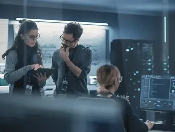 Pracownicy omawiający informacje na tablecie przy stanowisku komputerowym – planowanie i aktualizacja wersji procesów w systemie zarządzania workflow