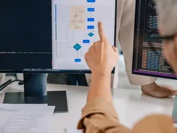Pracownik wskazujący informacje na monitorze komputera – omawianie możliwości systemu low-code przed rozpoczęciem wdrożenia