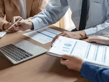 Pracownicy analizujący raporty i dane na laptopie przy biurku - weryfikacja dokumentacji w systemie DMS zgodnym z wymaganiami KNF i DORA