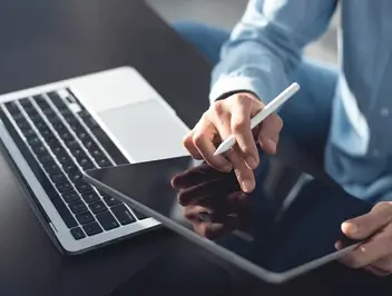 Dłonie mężczyzny obsługujące tablet obok laptopa – elektroniczne opiniowanie i zarządzanie umowami w firmie.