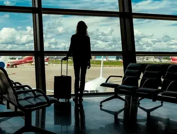Kobieta z walizką na lotnisku patrząca na samoloty - symbol planowania urlopu pracowniczego i zarządzania nieobecnościami w firmie.