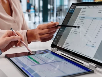 Dłoń kobiety wskazuje dane na laptopie, a druga osoba analizuje informacje na tablecie - wizualizacja wirtualnego drukowania faktur do PDF i pracy z cyfrowymi dokumentami