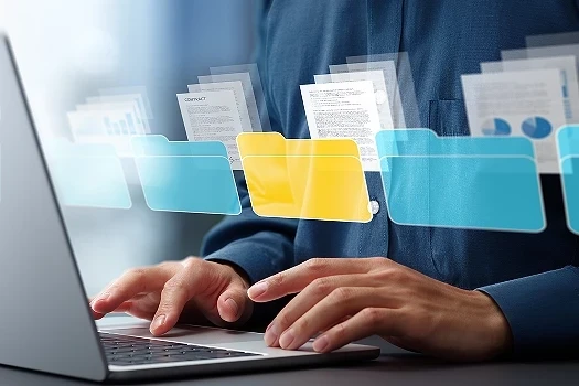 Dłonie na klawiaturze laptopa na pierwszym planie wirtualny interfejs z folderami jako symbol systemu DMS