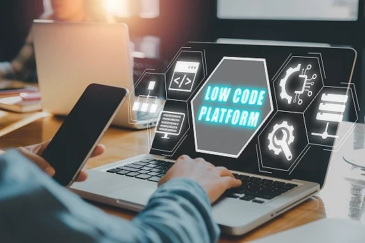 Dłoń pisząca na klawiaturze, w drugiej ręce telefon. Na ekranie laptopa napis Low code platform