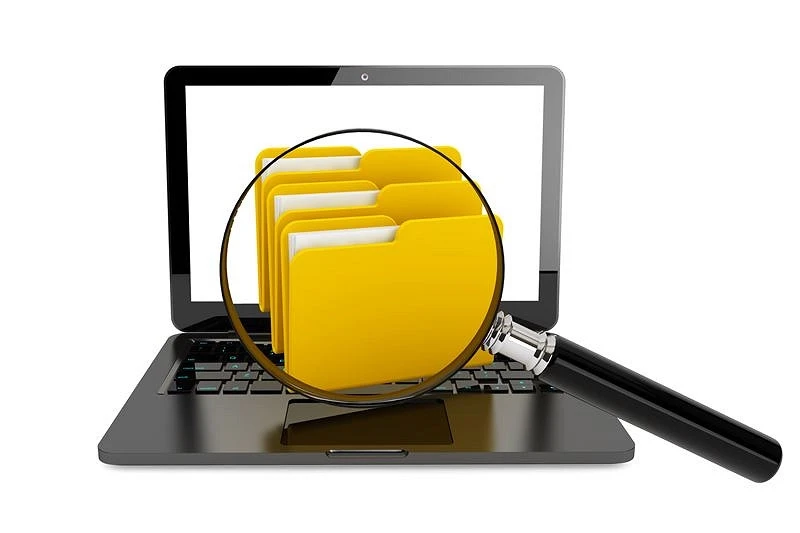 Lupa przybliżająca ikonę pliku z folderami na ekranie laptopa jako symbol cyfrowej firmowej bazy wiedzy