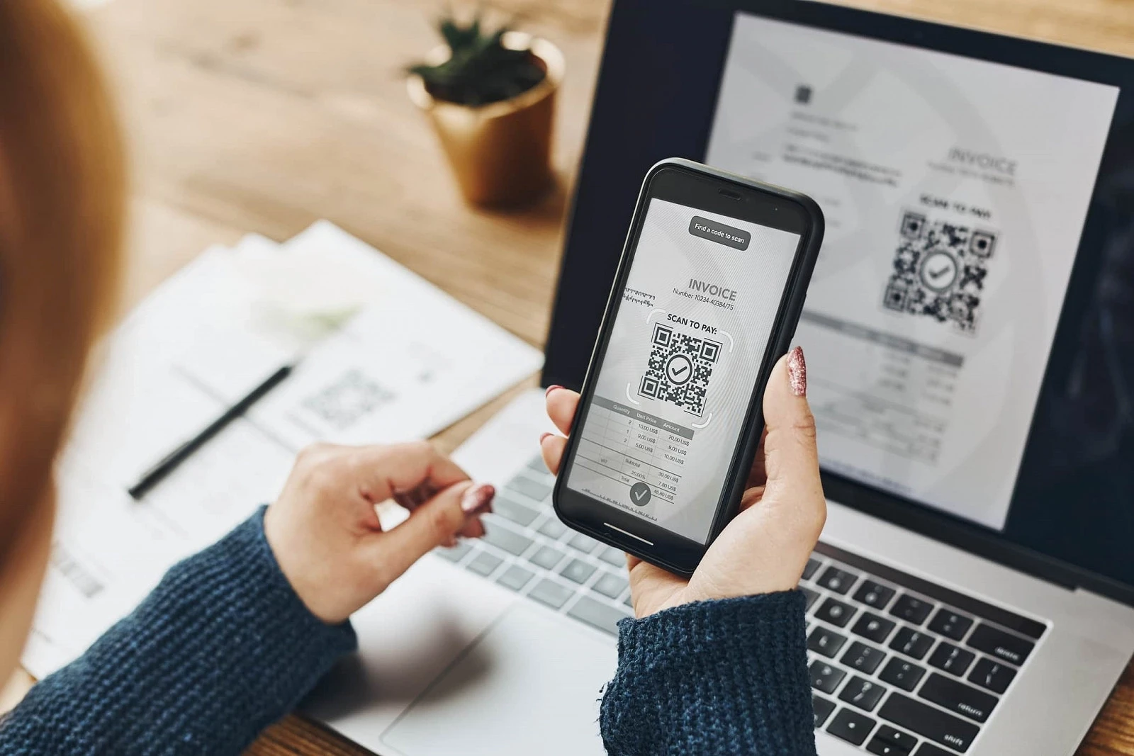 Kobieta trzymająca telefon przed ekranem laptopa, na obu ekranach widać kod QR nawiązujące do wirtualnego drukowania faktur