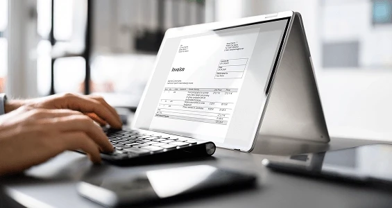 Dłonie przy na laptopie, na ekranie widoczna faktura - automatyzacja obiegu faktur – finanse i księgowość