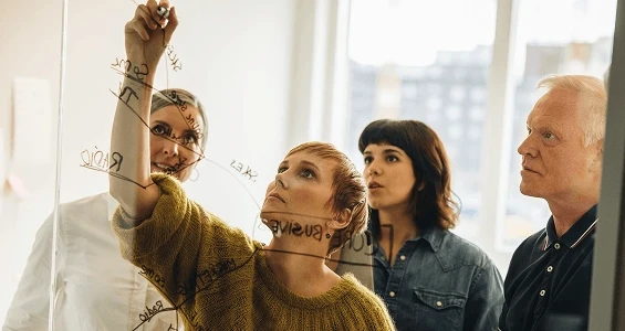 Pracownicy patrzą na kobietę rysującą schemat wdrażania dojrzałości procesowej w firmie