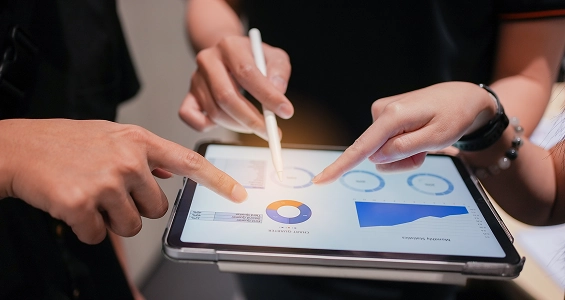 Pracownicy działu finansowego weryfikujący wskaźniki i wykresy na interaktywnym dashboardzie na tablecie.