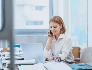 Pracownica biura spółdzielni mieszkaniowej obsługująca zgłoszenie mieszkańca przez telefon i laptopa