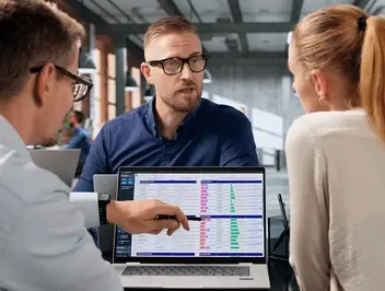 Trzy osoby w biurze analizują dane na ekranie laptopa, co może ilustrować weryfikację informacji w ramach cyfrowego paszportu produktu