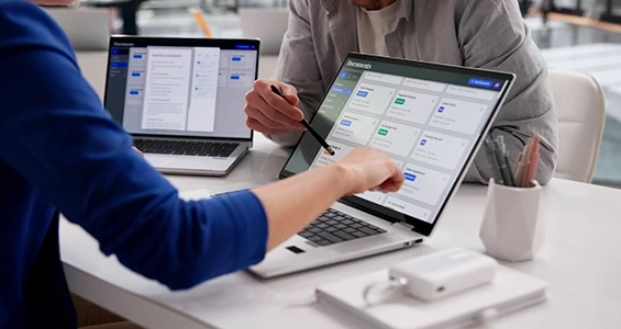 Pracownicy omawiający zadania w panelu cyfrowego systemu workflow na ekranie laptopa